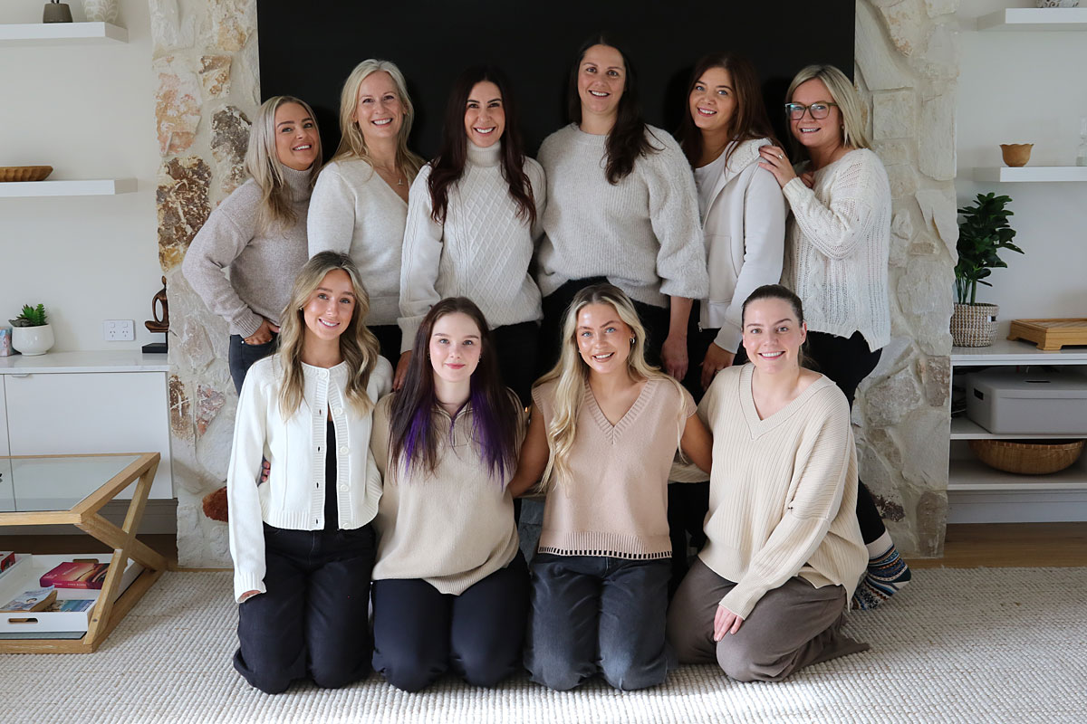 10 staff members in beige jumpers on a retreat, smiling looking at the camera standing in front of a fireplace
